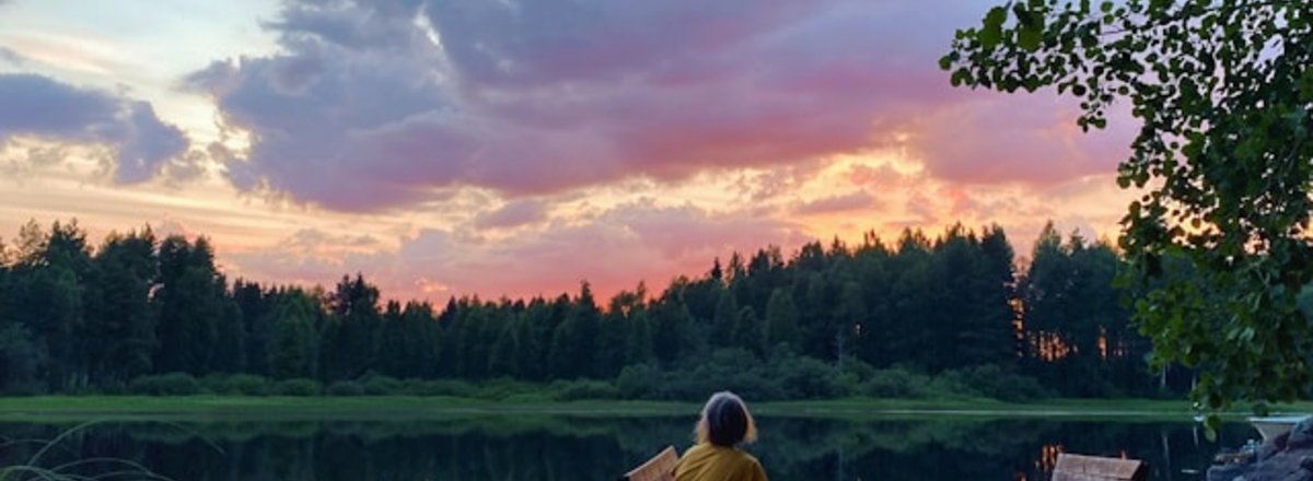 Woman on a chair at a lake in the woods at sunset