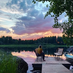 Woman on a chair at a lake in the woods at sunset